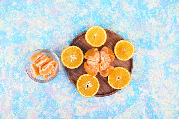 Arance e mandarini a fette isolati su un piatto di legno e in una tazza di vetro