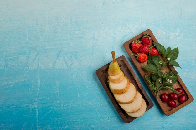 Sliced pears with strawberries and mulberries in wooden platters in the right side