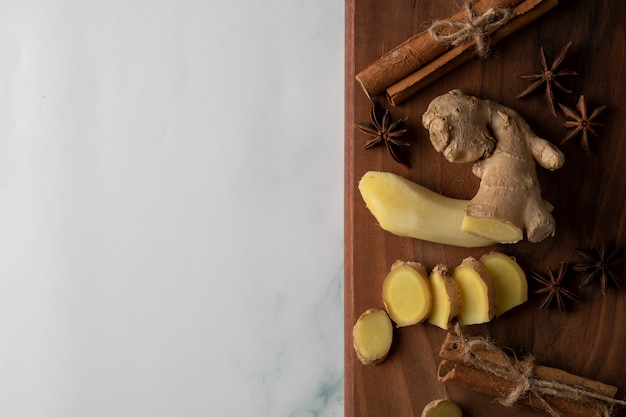 sliced and peeled ginger plants on a wooden board with anise and cinnamon sticks