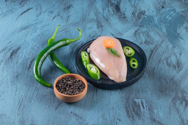 Sliced pepper and chicken breast on a plate next to spice bowl , on the blue surface.