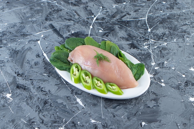 Tagliata di peperone, spinaci e petto di pollo su un piatto, sulla superficie di marmo.