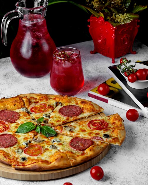 Нарезанная пицца пепперони с кусочками помидоров, сыром и соусом песто