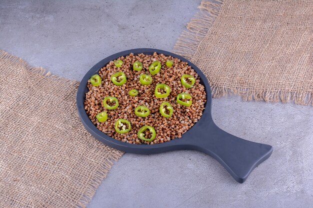 Free photo sliced peppers on top of a serving of buckwheat in a frying pan on marble background. high quality photo