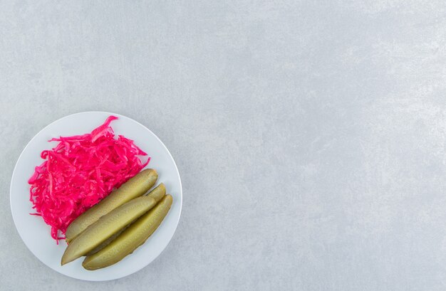 Sliced pickles cucumber next to sauerkraut on a plate on the marble surface