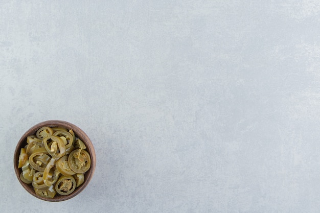 Sliced pickles jalapeno peppers in a bowl, on the marble surface