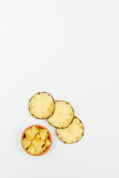 Sliced pineapple in a clay bowl on a white. top view.