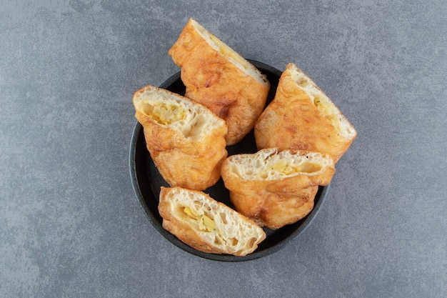 Sliced piroshki with potatoes in black bowl. 