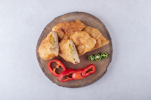 Sliced pirozhki and peppers on board on marble table.