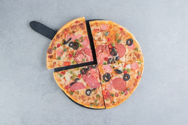Sliced pizza on a black board on marble 