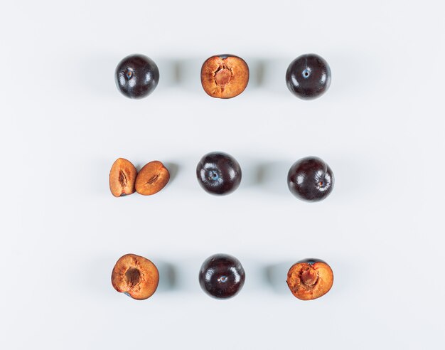 Sliced plums on white stucco background, flat lay.