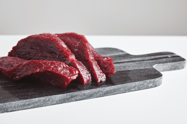 白いテーブルで隔離の大理石の石のまな板でスライスしたプレミアム生鯨肉ステーキ。クローズアップ、側面図