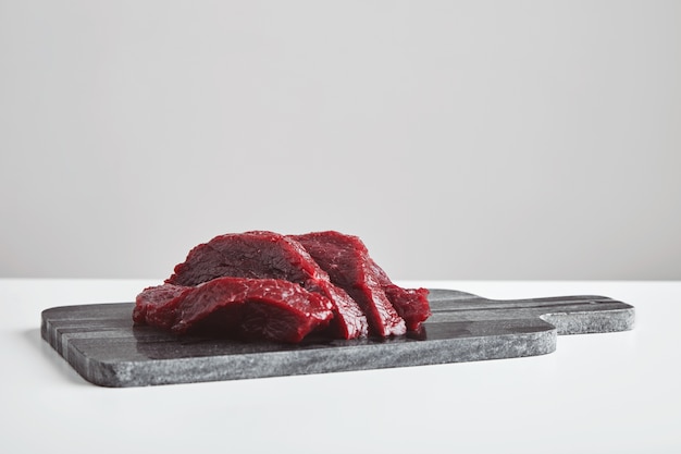 Sliced premium raw whale meat steak on marble stone cutting board isolated on white table. Close up