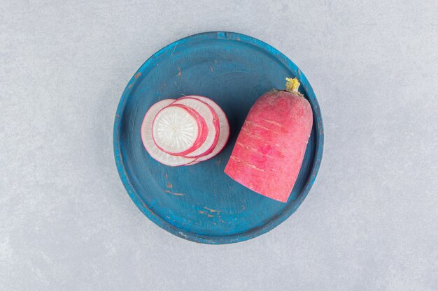 A sliced of radish on the blue tray, on the blue surface