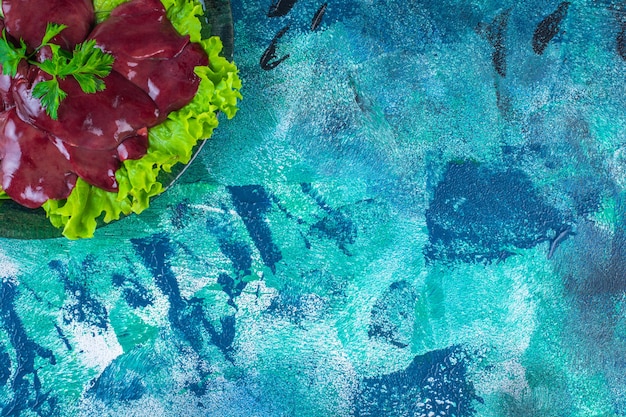 Sliced radish and offal on a lettuce leaf on the plate, on the blue background