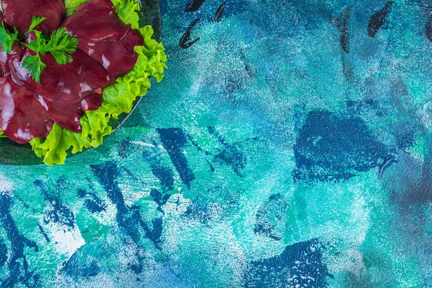 Нарезанный редис и субпродукты на листе салата на тарелке, на синем фоне