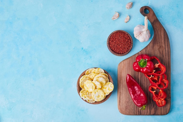 Sliced red chili and bell peppers on a wooden platter served with chips, top view.