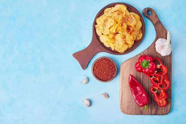 Sliced red chili and bell peppers on a wooden platter with spices and crackers aside.