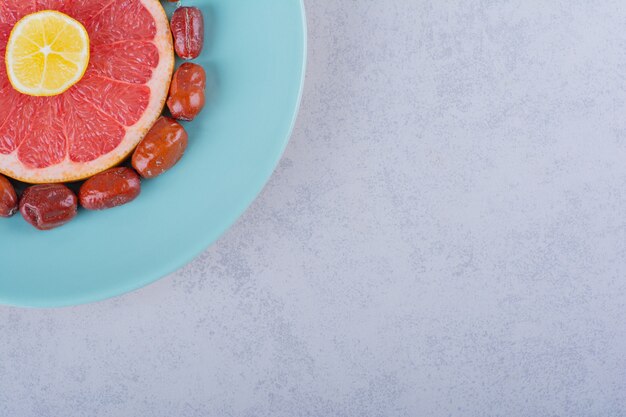 Sliced ripe grapefruit, lemon and silverberries on blue plate. 