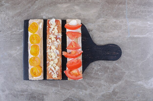 Sliced ripe and unripe tomatoes on crispy breads on the cutting board, on the marble background.