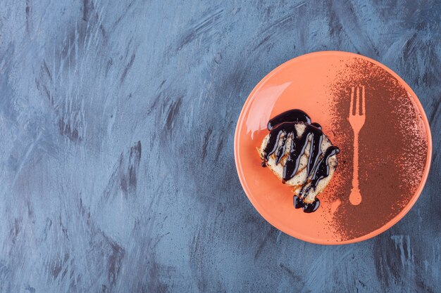 Sliced roll cake decorated with chocolate syrop on orange plate. 