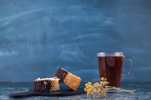 Sliced roll cake on wooden board with cup of tea on stone background. 