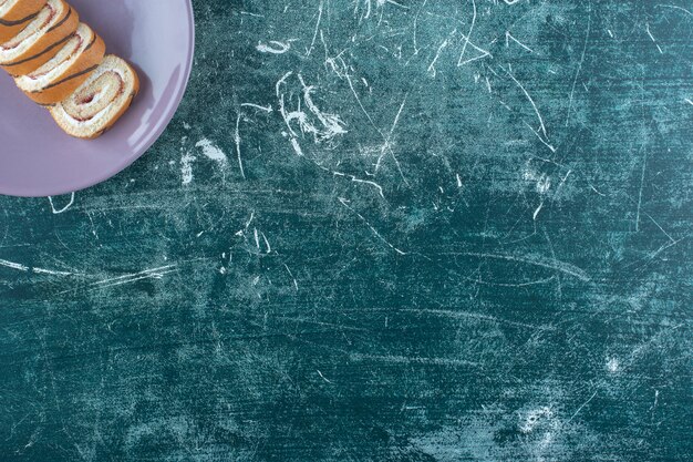 Sliced roll cakes on a plate, on the blue table. 