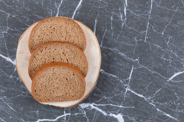 Нарезанный ржаной хлеб на разделочной доске над серым.