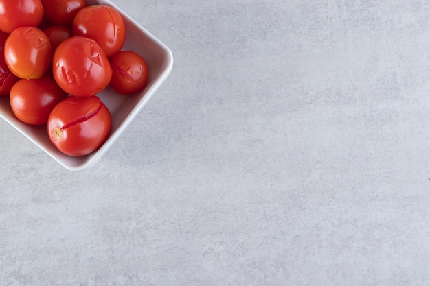 Sliced salty tomatoes in wooden bowl placed on stone background.