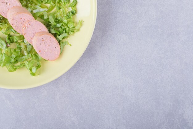 Sliced sausages and lettuce on yellow plate.