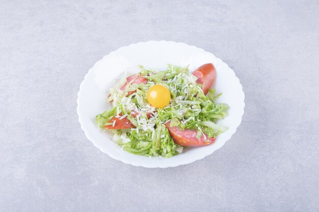 Sliced smoked sausages, lettuce and egg yolk in white bowl. 