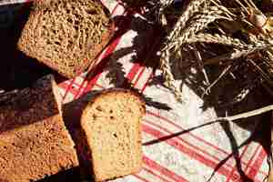 Free photo sliced sourdough bread on on rustic red gray kitchen towel and spikelets of wheat table top view natural sun light