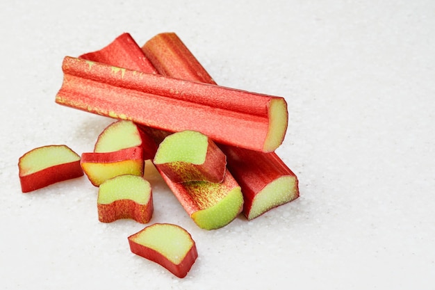 Free photo sliced stalk of rhubarb on a white marble background whole rhubarb sticks with a few pieces of chopped rhubarb isolated ingredients for making a pie