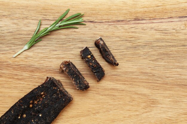 Sliced stick of biltong snack and rosemary seasoning on a wooden surface