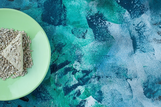 Sliced sunflower halva with seeds on the plate, on the marble table.