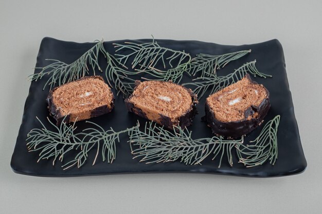 Foto gratuita rotolo di cioccolato dolce affettato su un piatto nero.