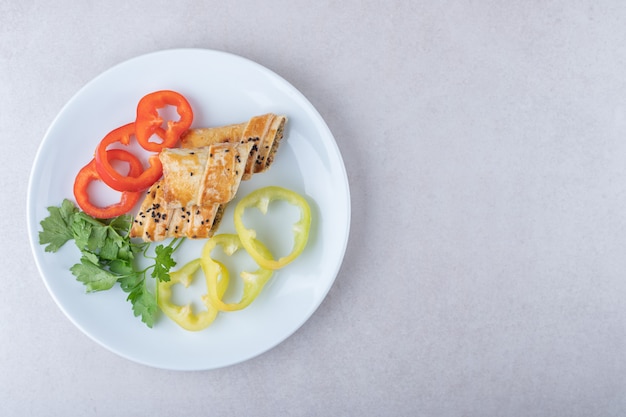 Нарезанный сладкий перец, петрушка и оладьи с мясом на тарелке, на мраморе.