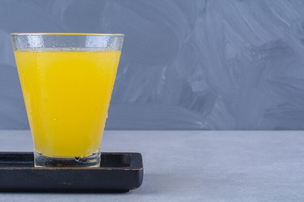 대리석 테이블에 있는 나무 접시에 있는 오렌지 주스 한 잔 옆에 얇게 썬 귤.