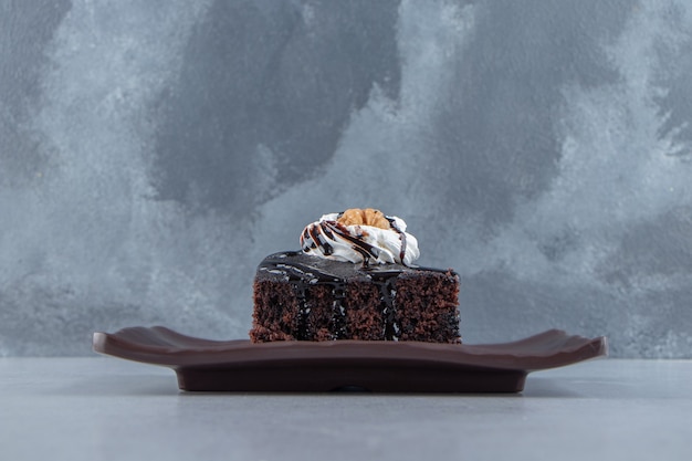 Sliced of tasty chocolate brownie with cream on dark plate