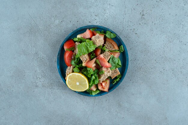Sliced tomato, bread, lemon and greens on blue plate.