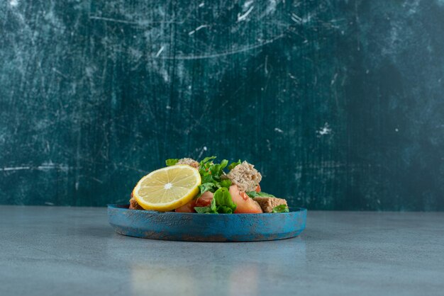 Sliced tomato, bread, lemon and greens on blue plate.