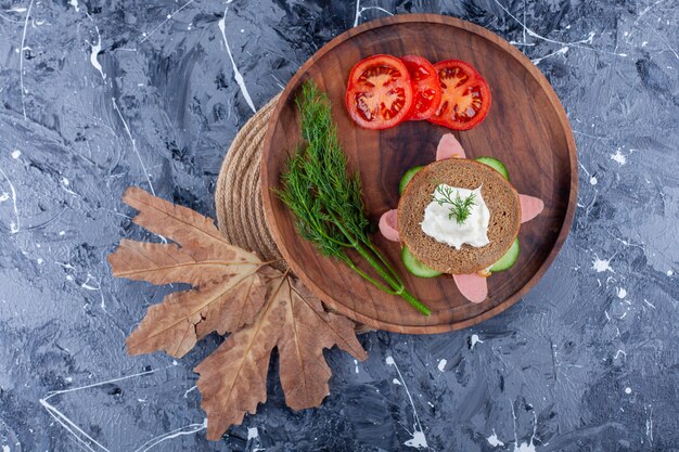 Sliced tomatoes, dill and sandwich on a board , on the blue surface.