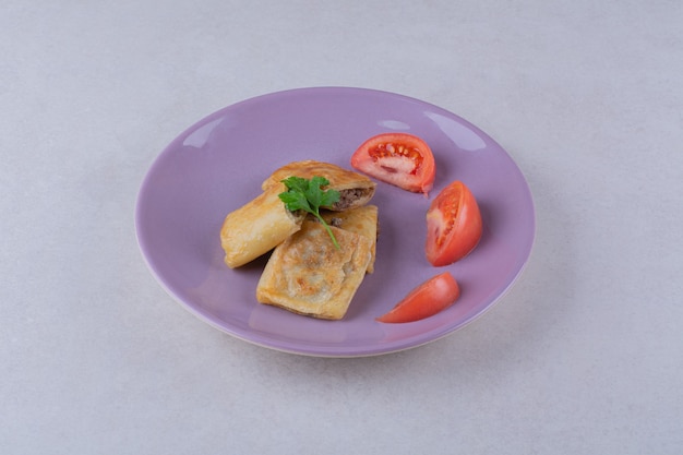 Нарезанные помидоры и блин с мясом на тарелке на темной поверхности