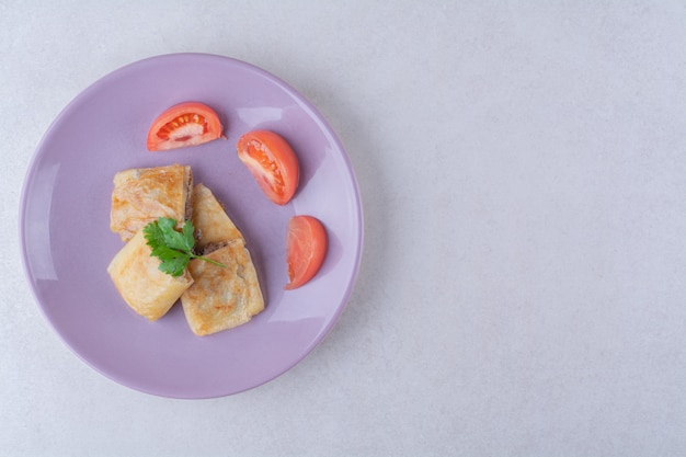 Sliced tomatoes and pancake with meat on plate on marble table.