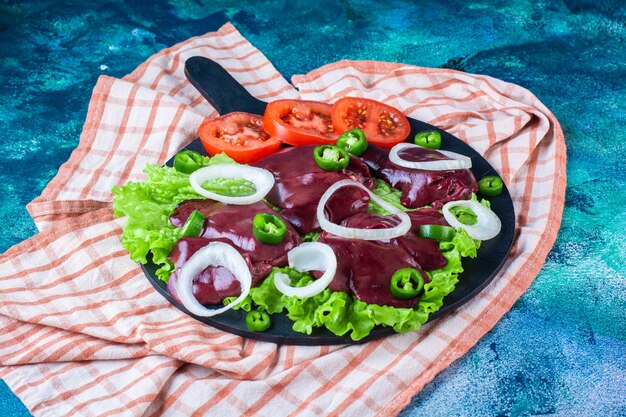 Sliced various vegetables and chicken livers on the cutting board on the tea towel