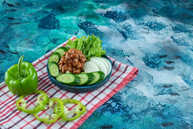 Sliced vegetables and baked beans on a wooden plate on a towel , on the blue table. 