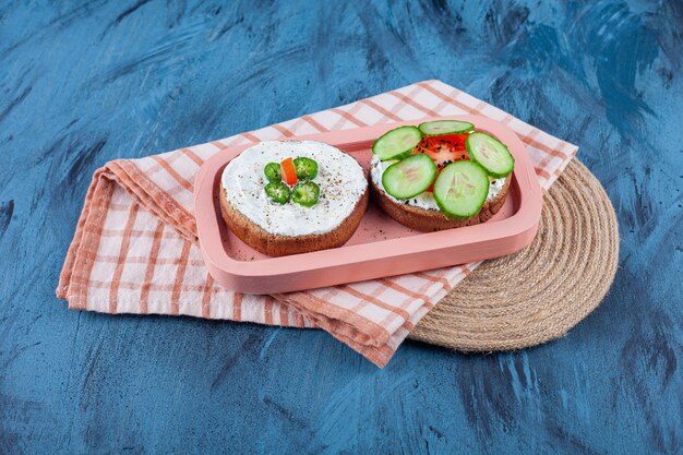 Sliced vegetables on cheese breads in board on towel on trivet, on the blue table.