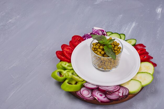 Sliced vegetables and herbs in a white plate on blue table.