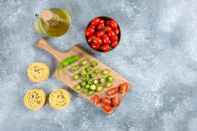 Sliced vegetables, olive oil and pasta nests on marble background.