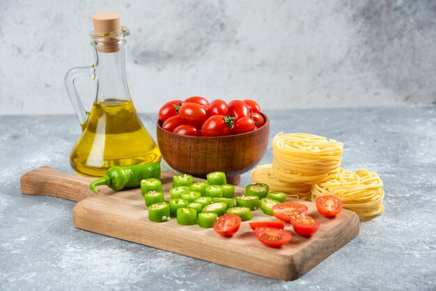 Sliced vegetables, olive oil and pasta nests on marble background.