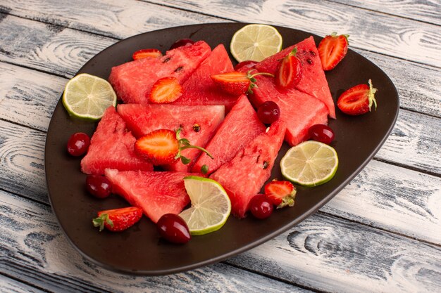 sliced watermelon with lemon strawberries inside brown plate on grey